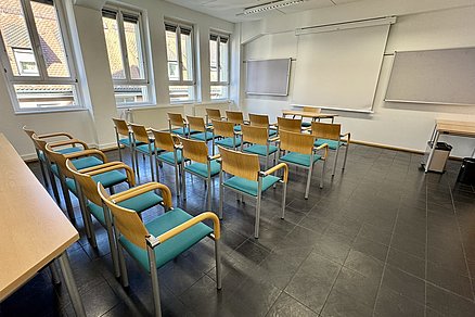 Vier Stuhlreihen zu je fünf Stühlen blicken auf einen Tisch mit einem Stuhl an der Stirnseite