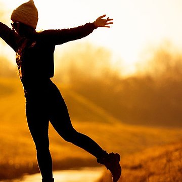Im herbstlichen Abendlicht balanciert eine junge Frau auf einem schmalen Steg über einem Bach.