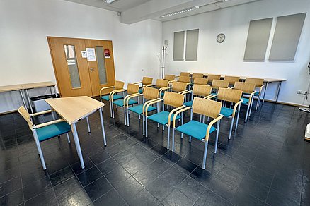 Vier Stuhlreihen zu je fünf Stühlen blicken auf einen Tisch mit einem Stuhl an der Stirnseite