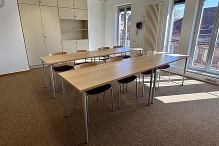 Zwei Tischreihen hintereinander zu je vier Stühlen